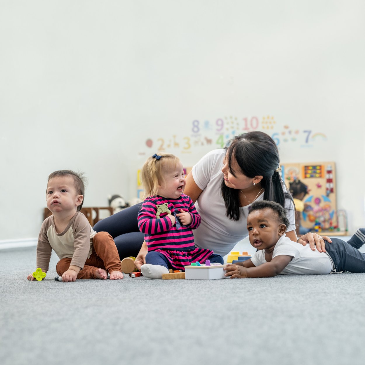 3 infants playing on the floor with a child care worker