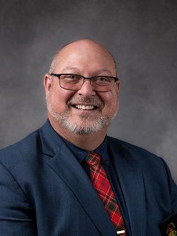 Deputy Warden Jerry Acchione, wearing a dark blue suit with a red, green and yellow plaid tie. 